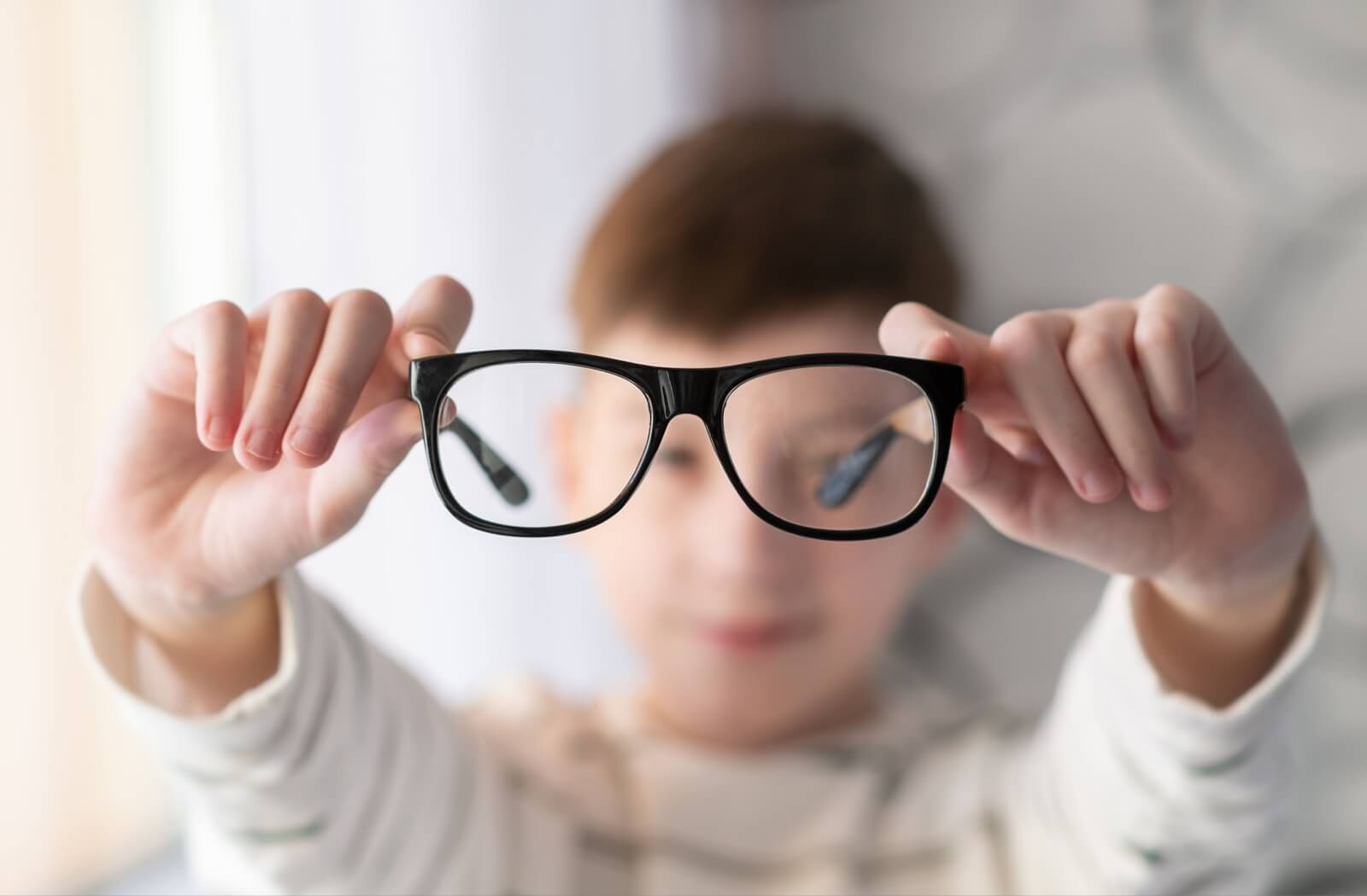 Child holding eyeglasses, illustrating myopia glasses designed for nearsighted vision correction.