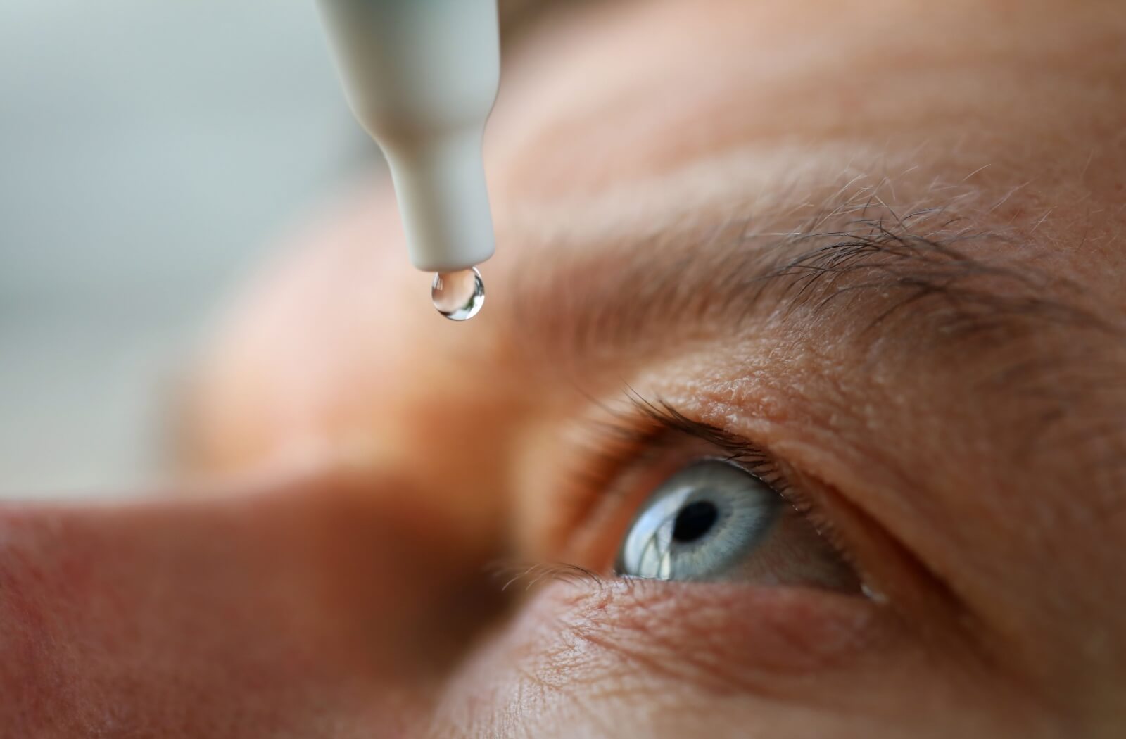 A macro close-up of a medicinal drop falling from a bottle toward an eye, highlighting Atropine eye drop treatment for managing childhood myopia and nearsightedness.